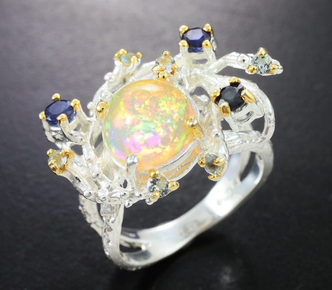 Серебряное кольцо с кристаллическим эфиопским опалом, синими сапфирами и голубыми топазами